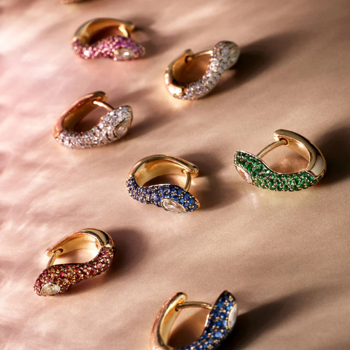 Gold hoop earrings with colorful gemstones on a pink fabric background