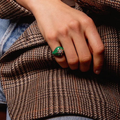 Hand wearing a green gemstone ring on a textured fabric background