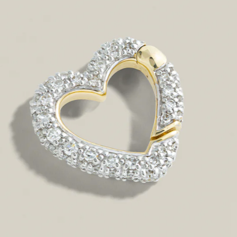 Heart-shaped jewelry piece with gold and clear gemstones on a beige background