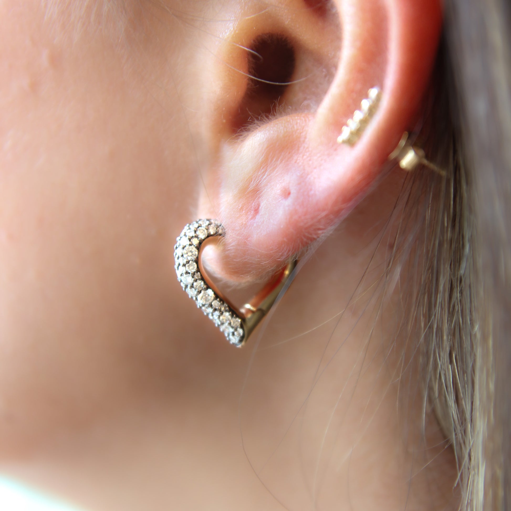 Close-up of an ear wearing a gold heart-shaped earring with clear stones.