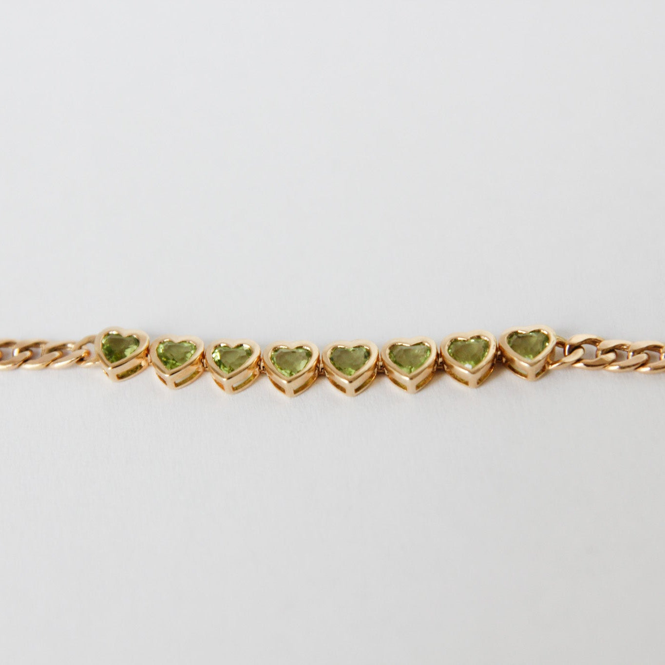Gold bracelet with heart-shaped green stones on a light gray background
