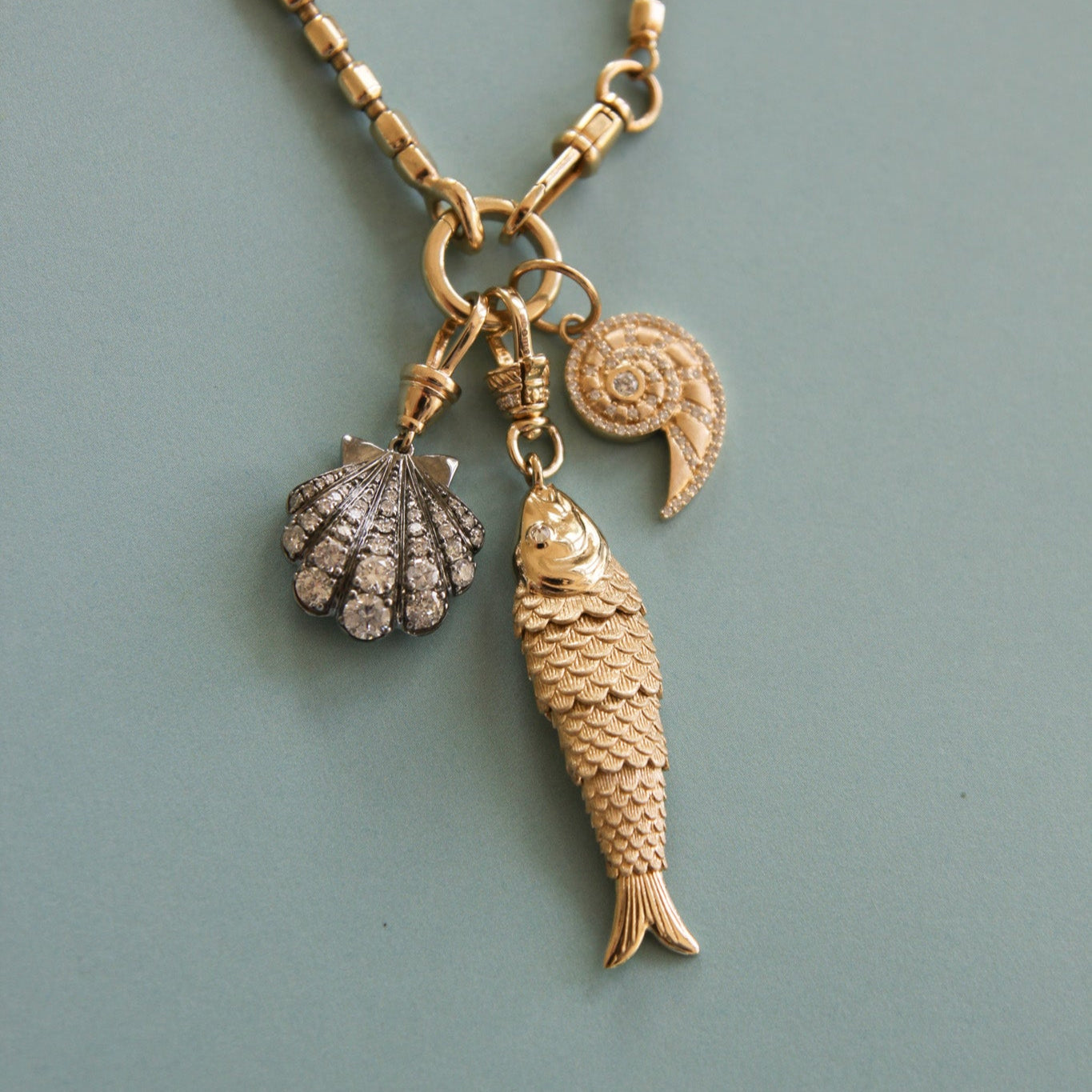 Gold necklace with fish and shell pendants on a light blue background