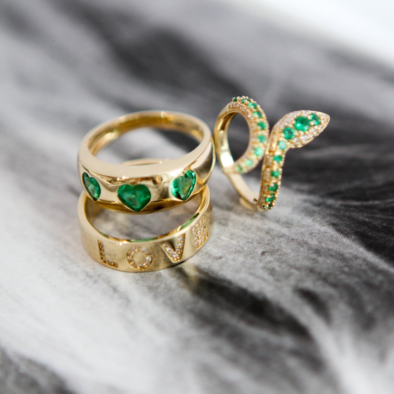 Gold rings with green gemstones on a marble surface