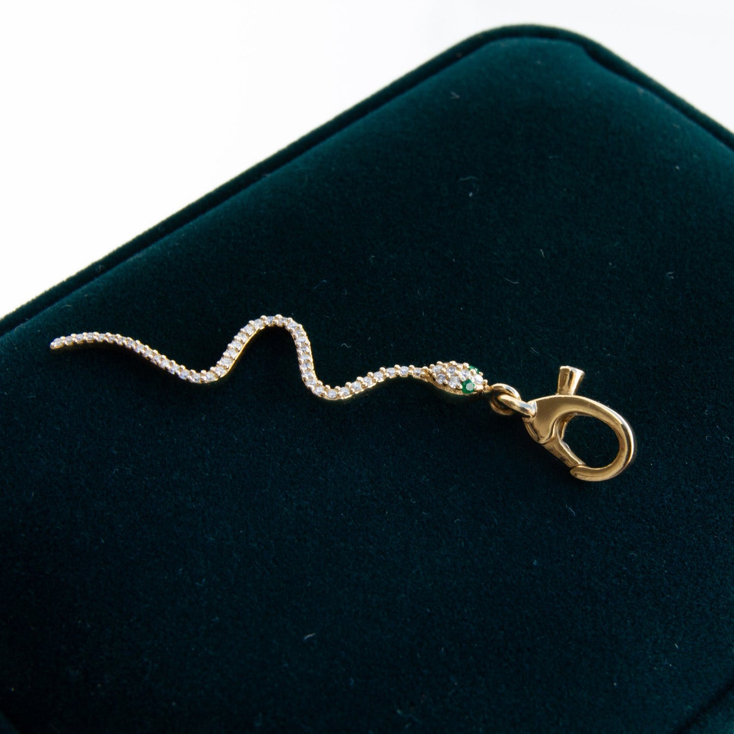 Gold serpent charm with emerald eyes on a dark green velvet surface