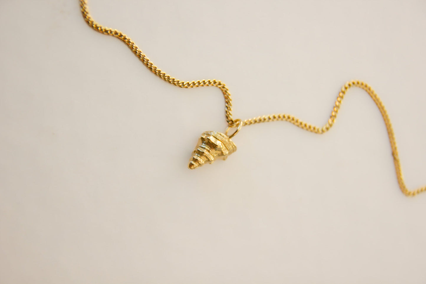 Gold necklace with a conical pendant on a beige background