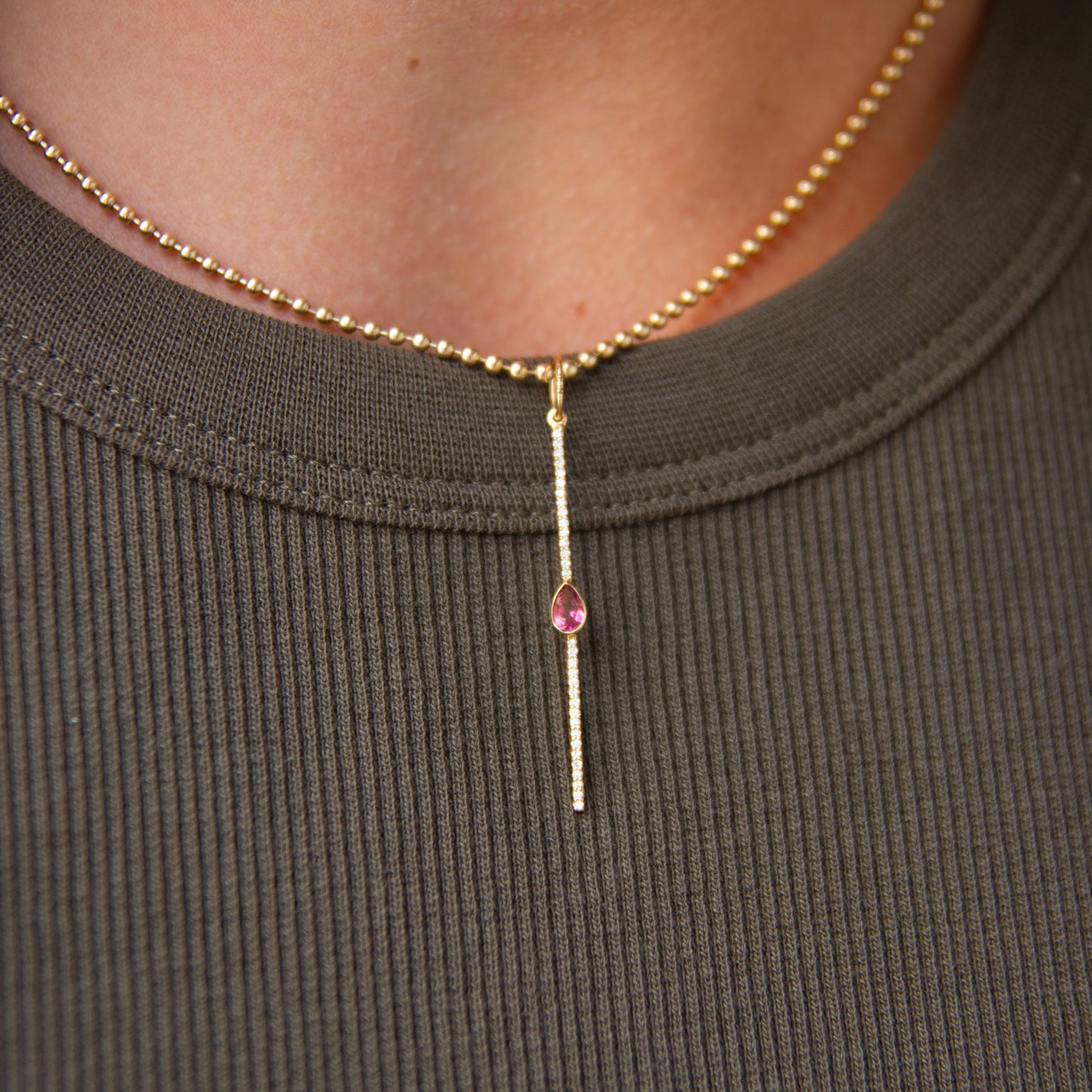 Necklace with a pink gemstone on a person wearing a brown ribbed shirt