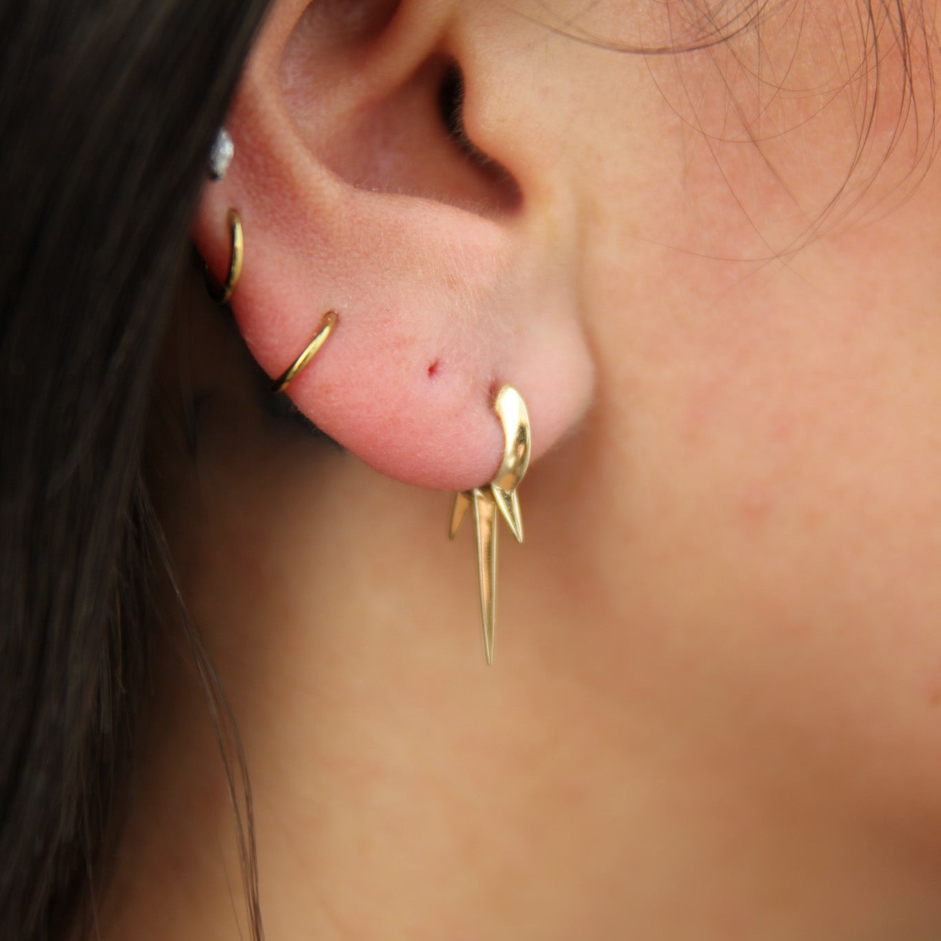 Close-up of an ear with gold triple dagger spiked earrings and a visible piercing.