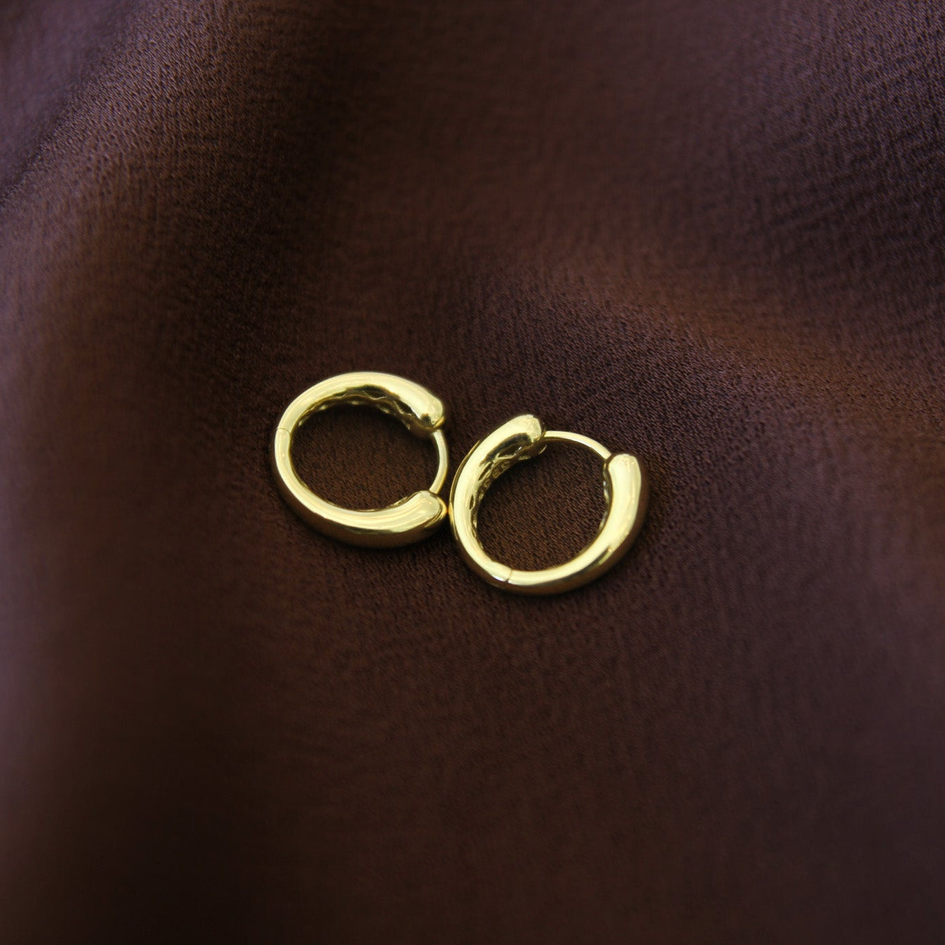 Two gold hoop earrings on a brown leather surface
