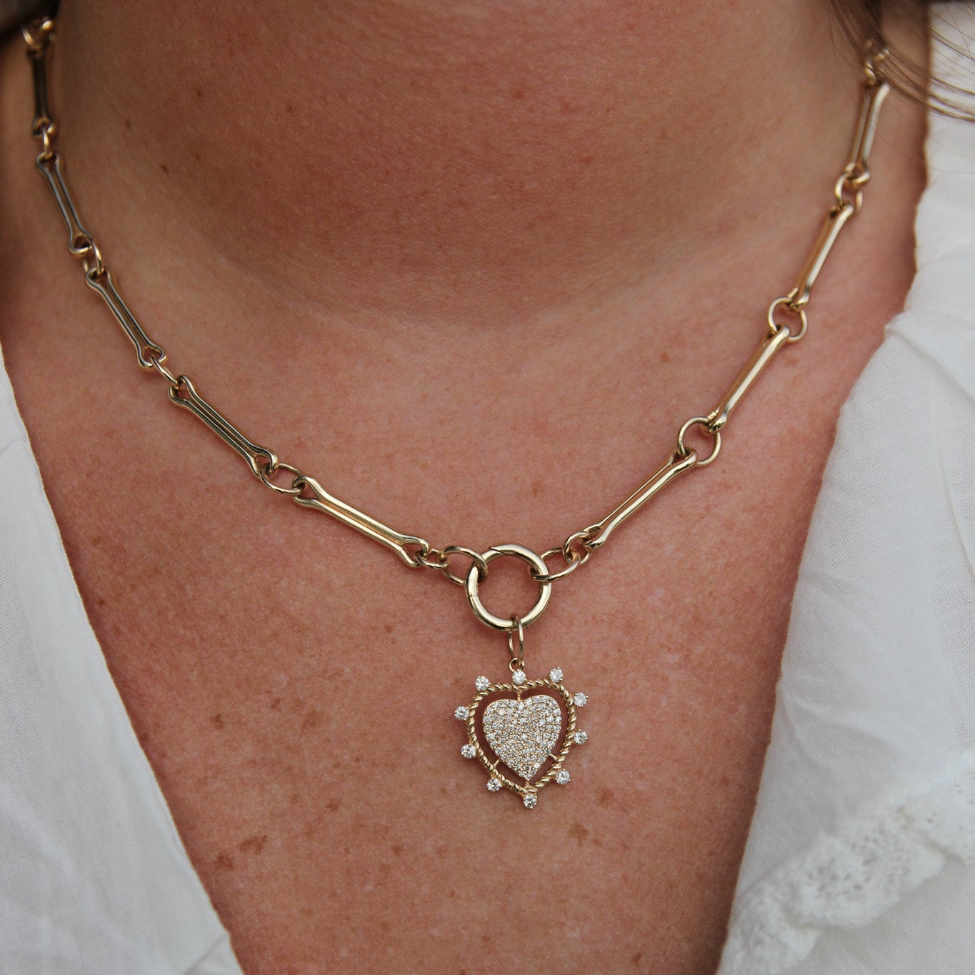 Gold chain necklace with a heart pendant worn by a person in a white shirt.