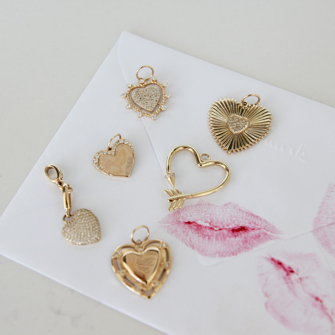 Gold heart-shaped jewelry charms on a white card with pink lip prints