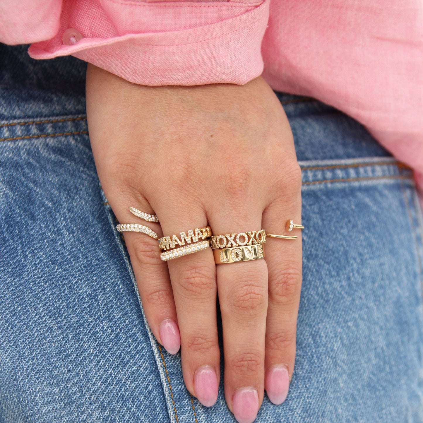 Hand wearing multiple gold rings with various inscriptions on a denim background