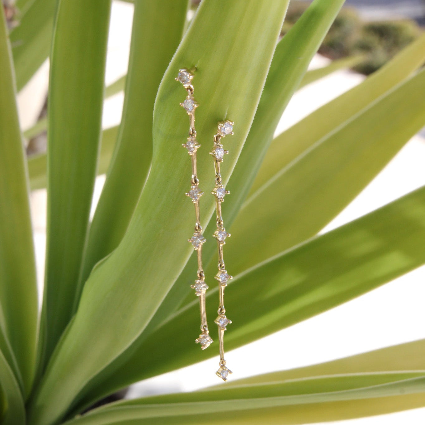 Gold earrings with gemstones on a green leaf background