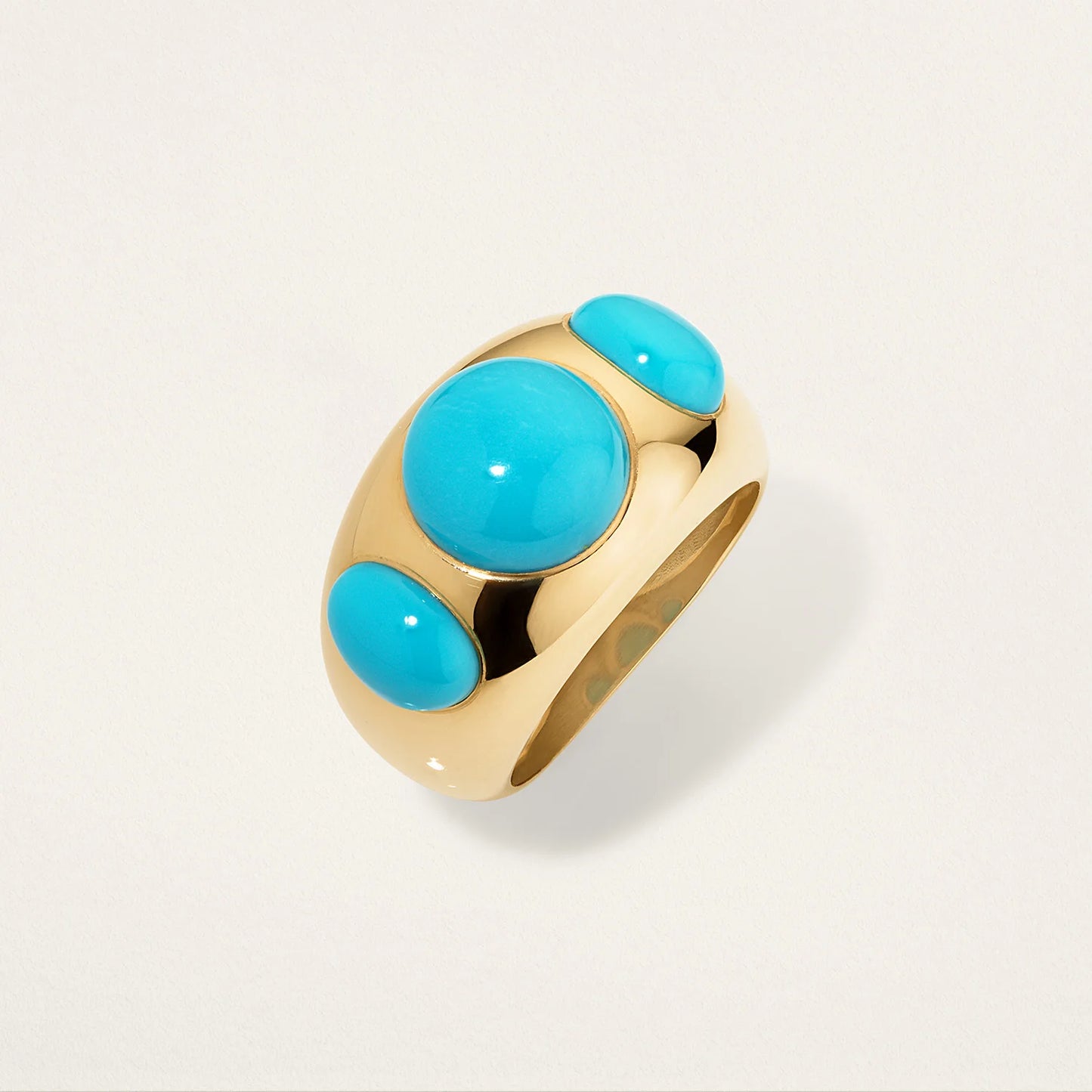 Gold ring with turquoise stones on a light gray background