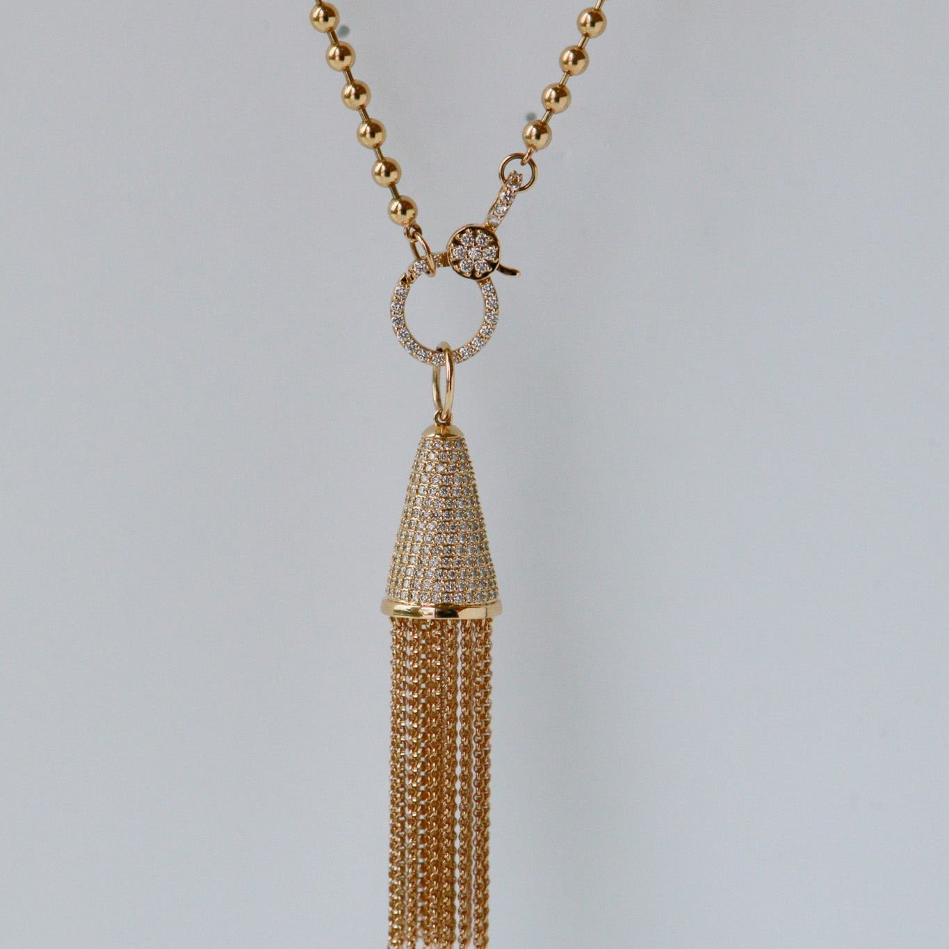 Gold necklace with a tassel pendant on a light gray background