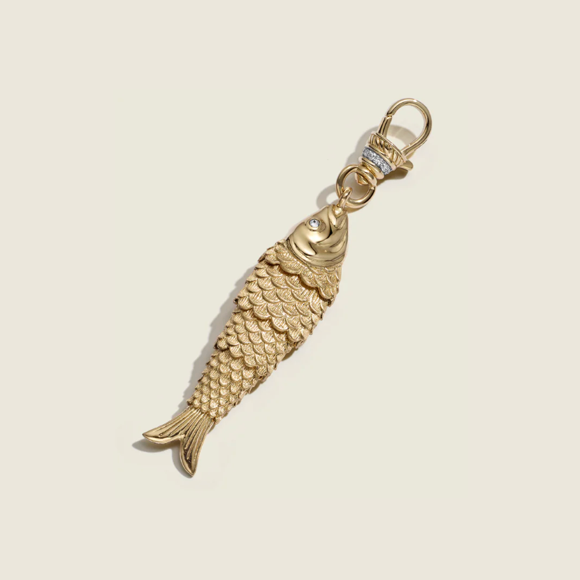Gold fish-shaped keychain on a beige background