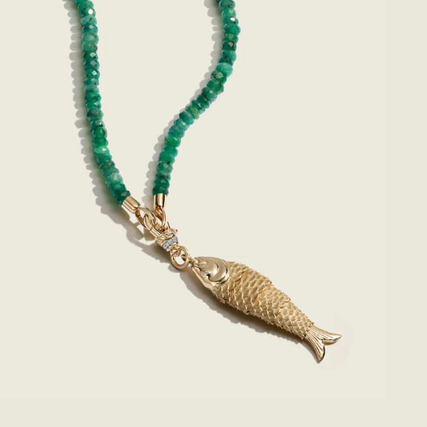 Necklace with green beads and a gold fish pendant on a beige background