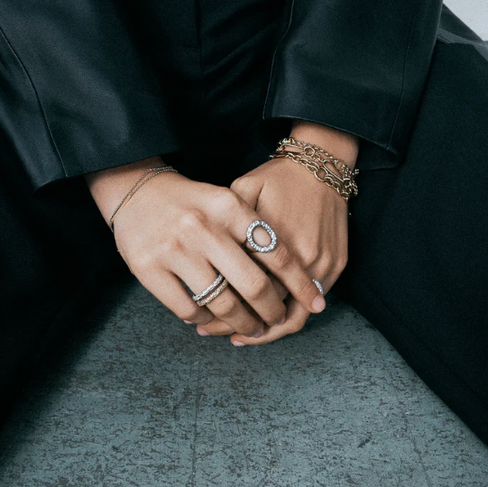 Close-up of hands with multiple rings and bracelets on a dark surface