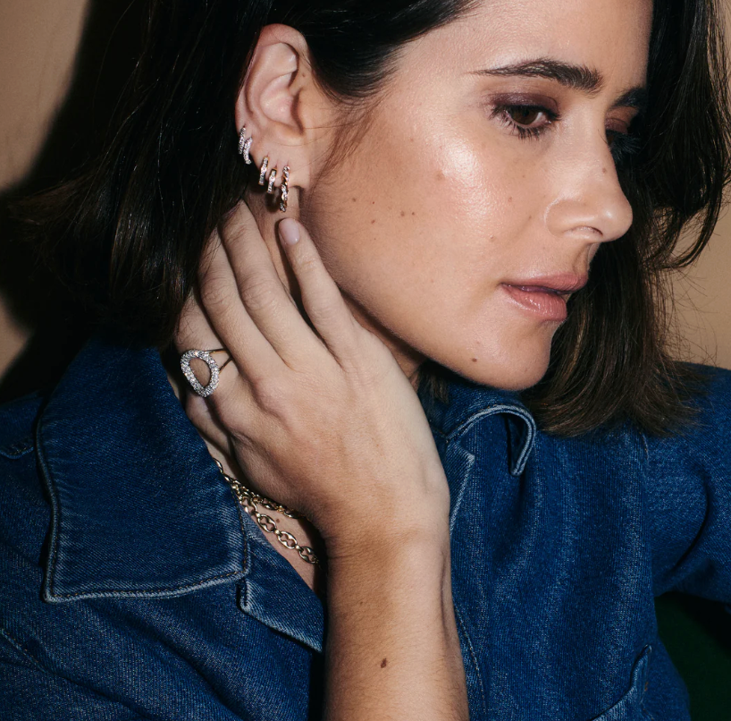 Close-up of a woman wearing earrings and a ring, with a neutral background