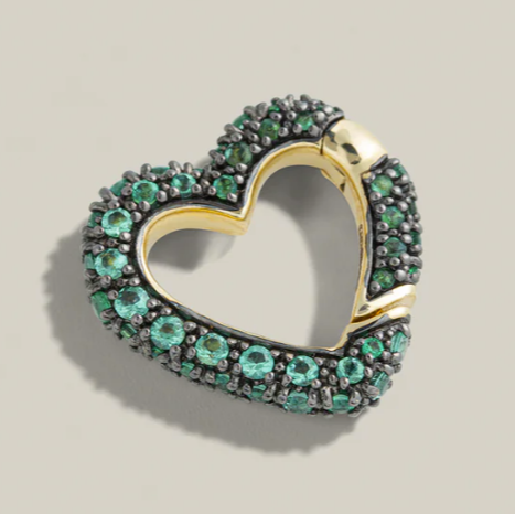 Heart-shaped jewelry piece with green gemstones and gold accents on a beige background