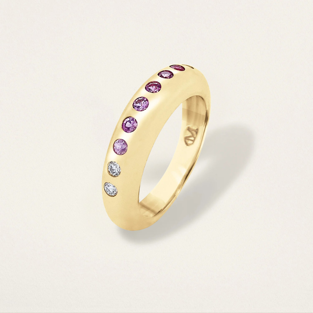 Gold ring with purple and clear gemstones on a light gray background