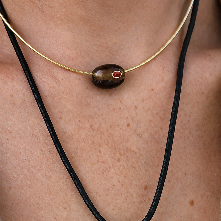 Necklace with a black pendant and red gemstone on a person's neck