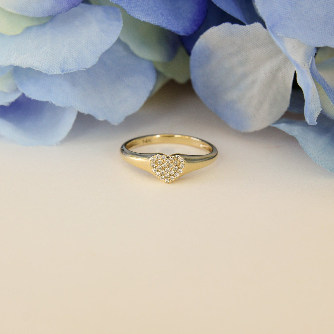 Gold ring with heart design on a light background with blue flowers
