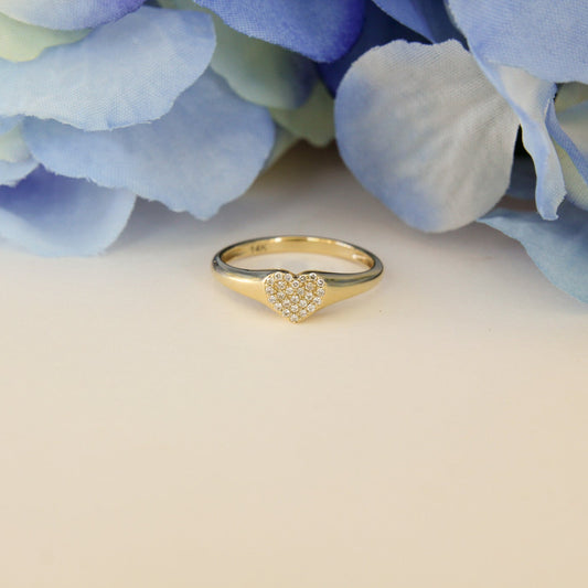 Gold ring with heart design on a light background with blue flowers