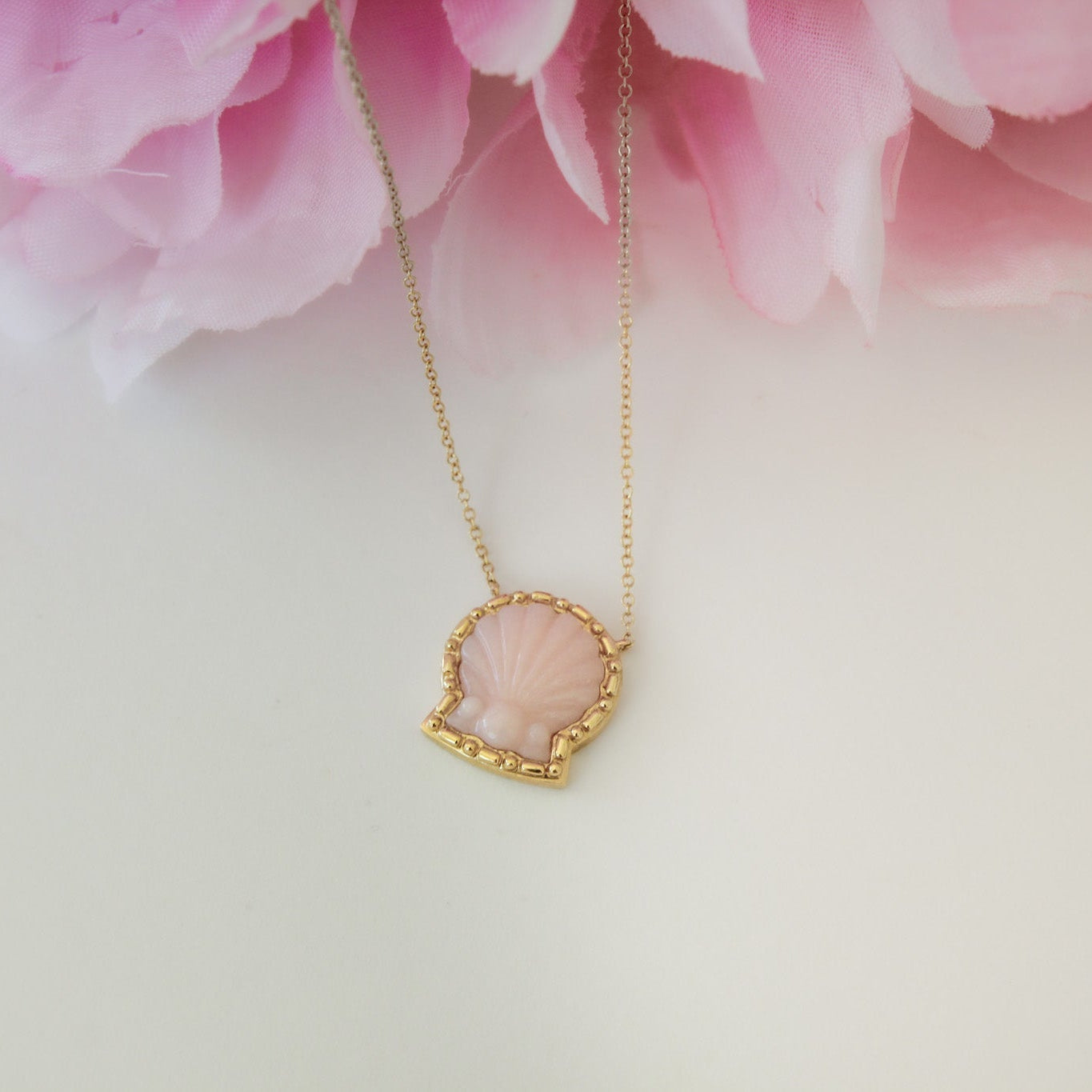 Gold necklace with a pink pendant against a soft pink floral background
