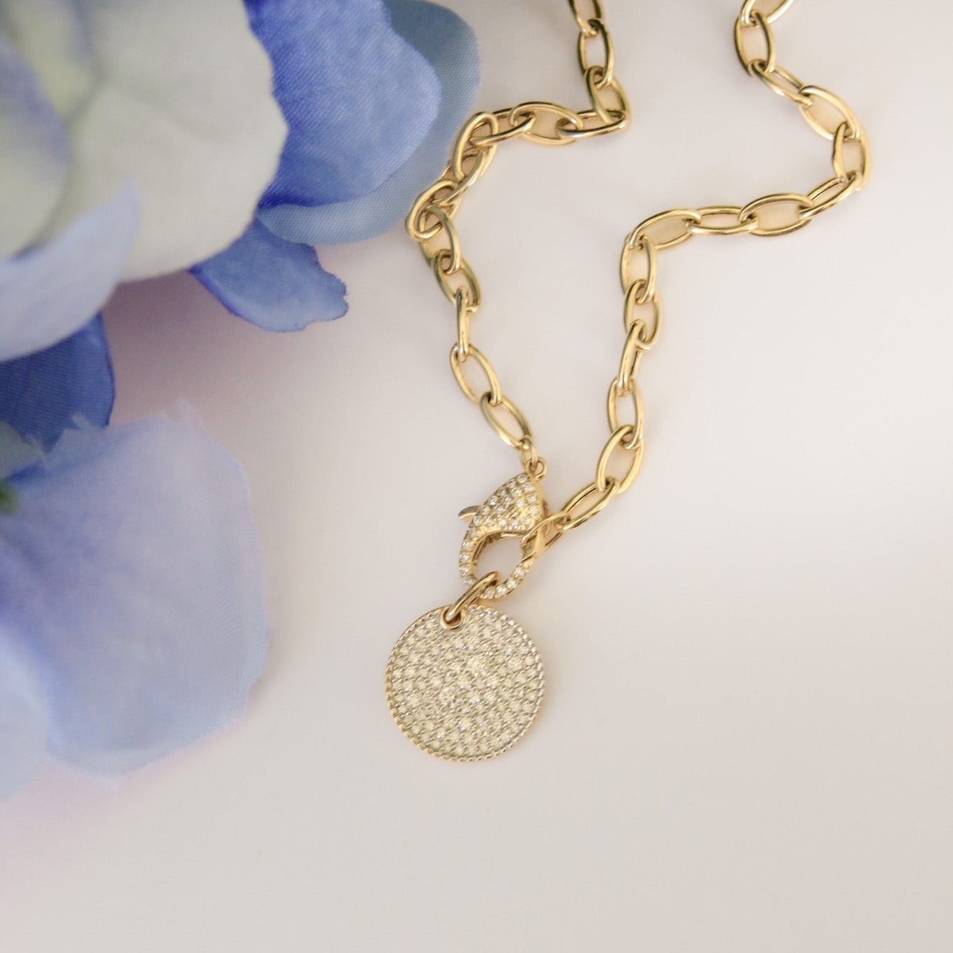 Gold necklace with a round pendant on a white surface with blue flowers in the background