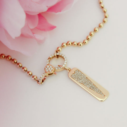 Gold necklace with a tag pendant on a pink floral background