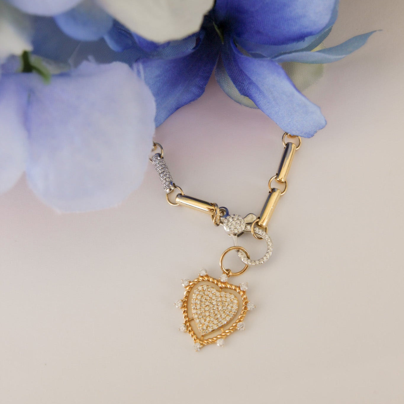 Gold heart-shaped charm on a bracelet with blue flowers in the background