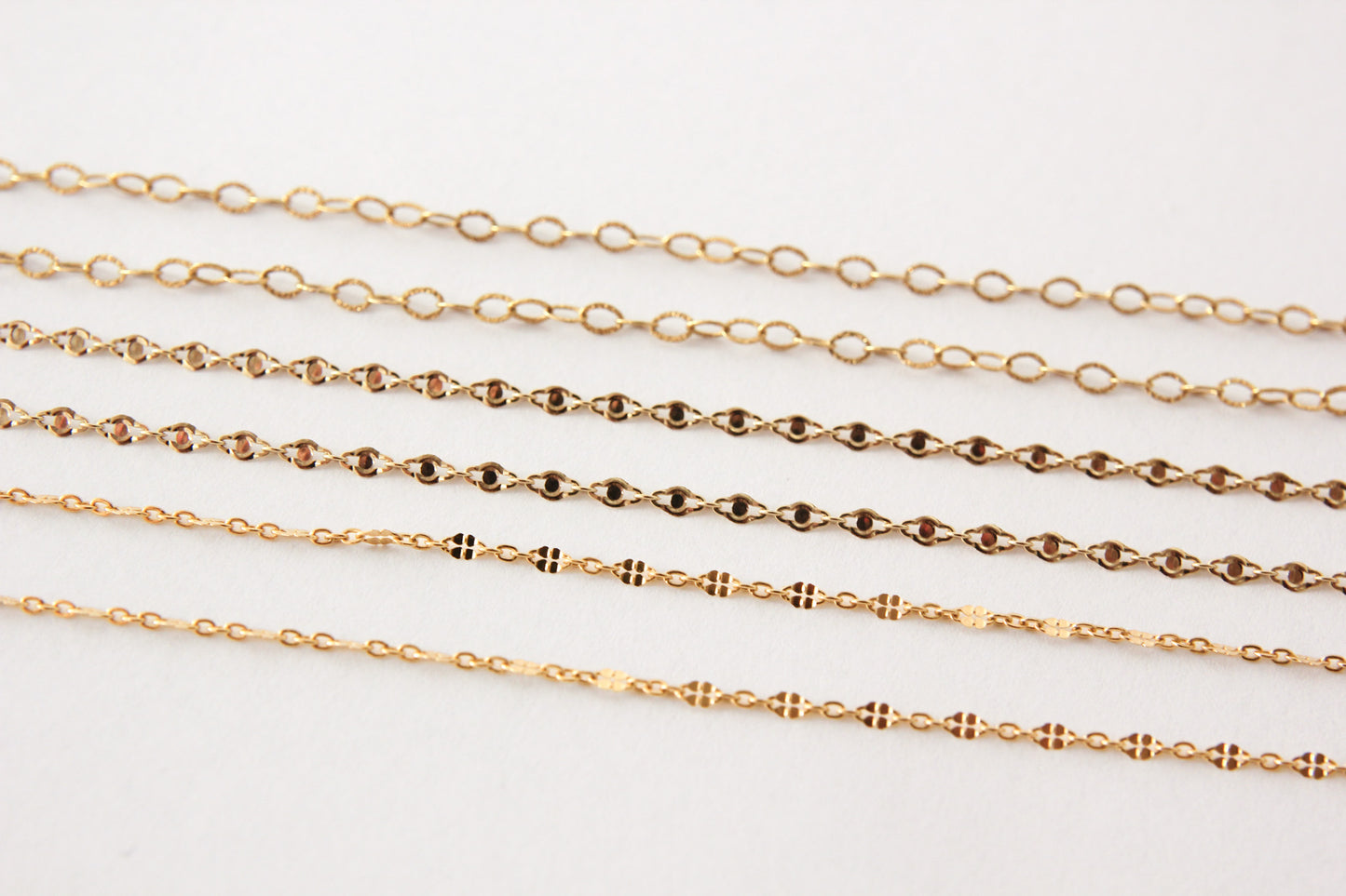 Gold chains of different thicknesses on a light gray background