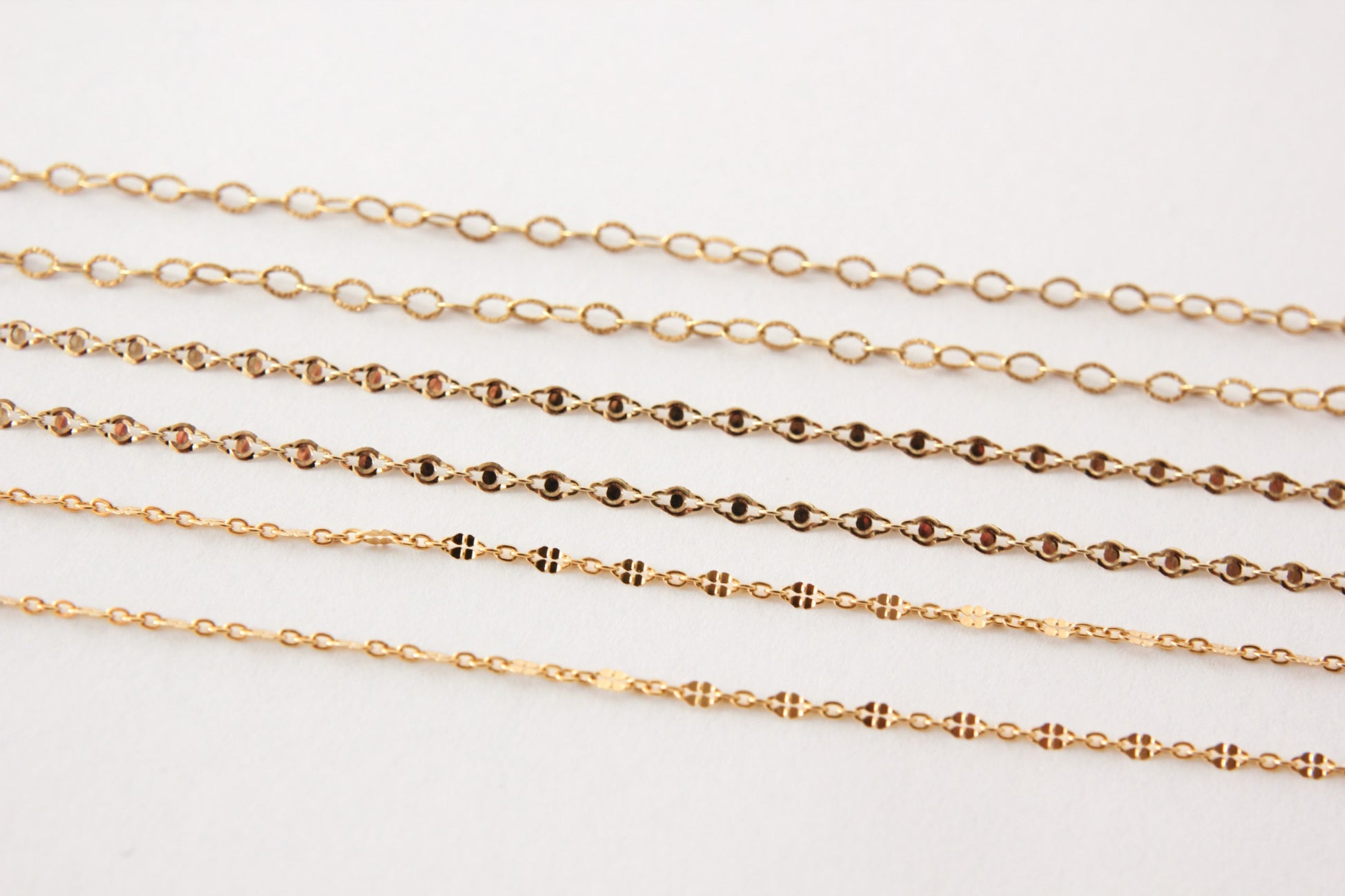 Gold chains of different thicknesses on a light gray background