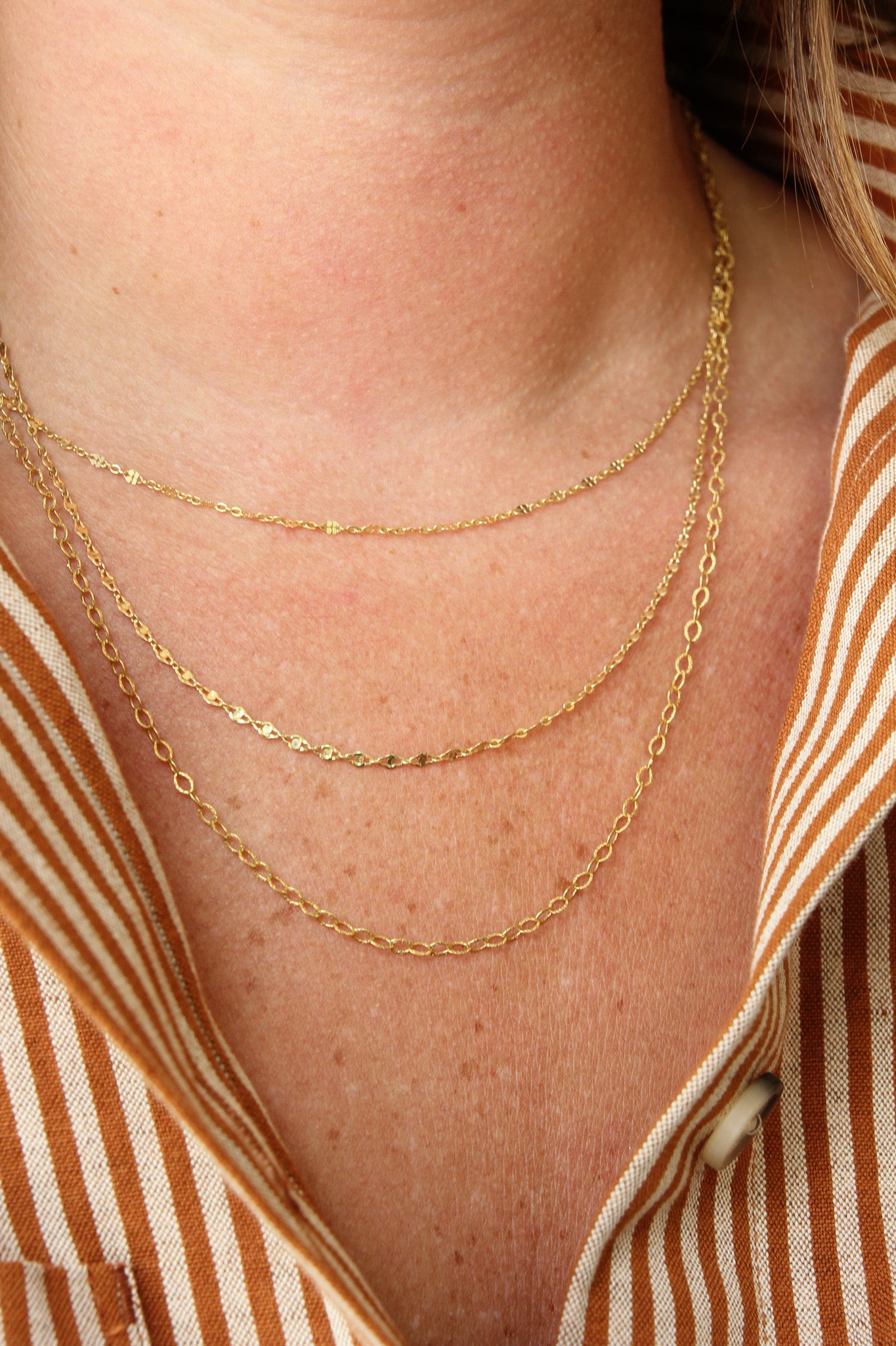 Close-up of a person wearing two gold necklaces with a striped shirt.