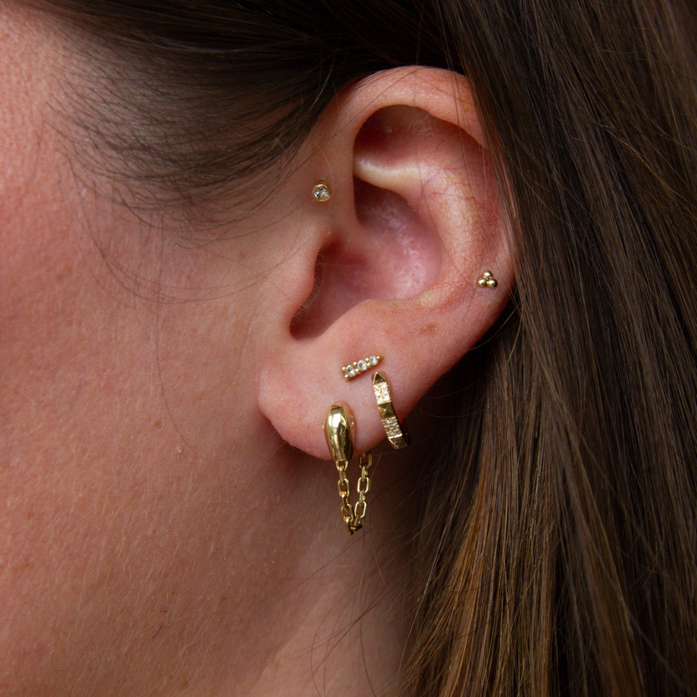 Close-up of an ear with gold earrings and a hoop earring.