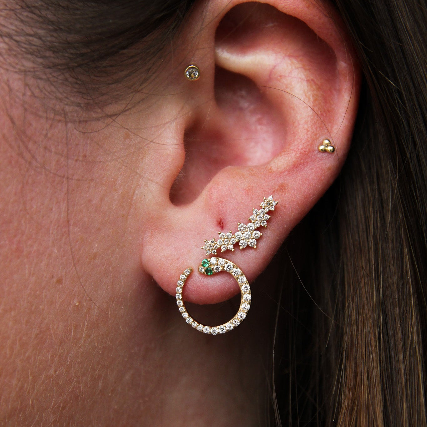 Close-up of an ear wearing a gold hoop earring with green gemstones.
