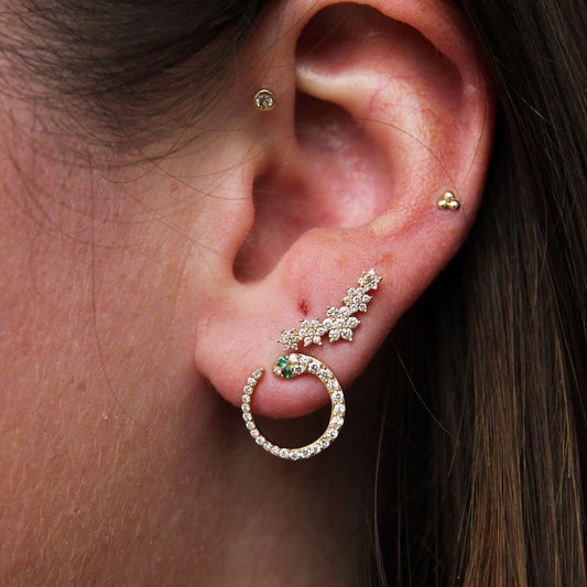 Close-up of an ear wearing a gold hoop earring with green gemstones.