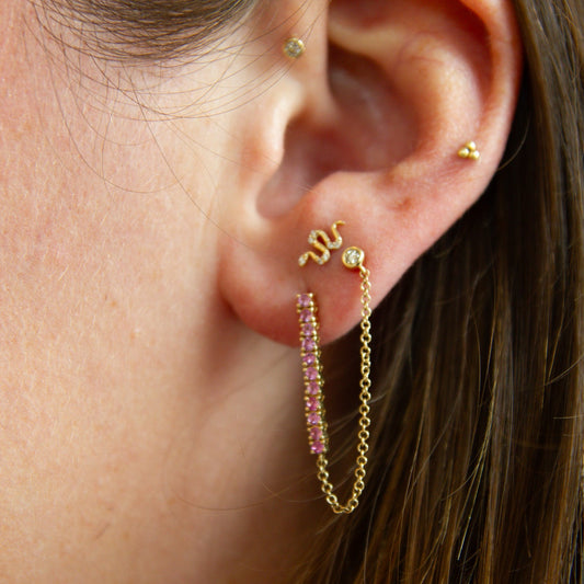Close-up of an ear with gold hoop earrings and pink gemstones.