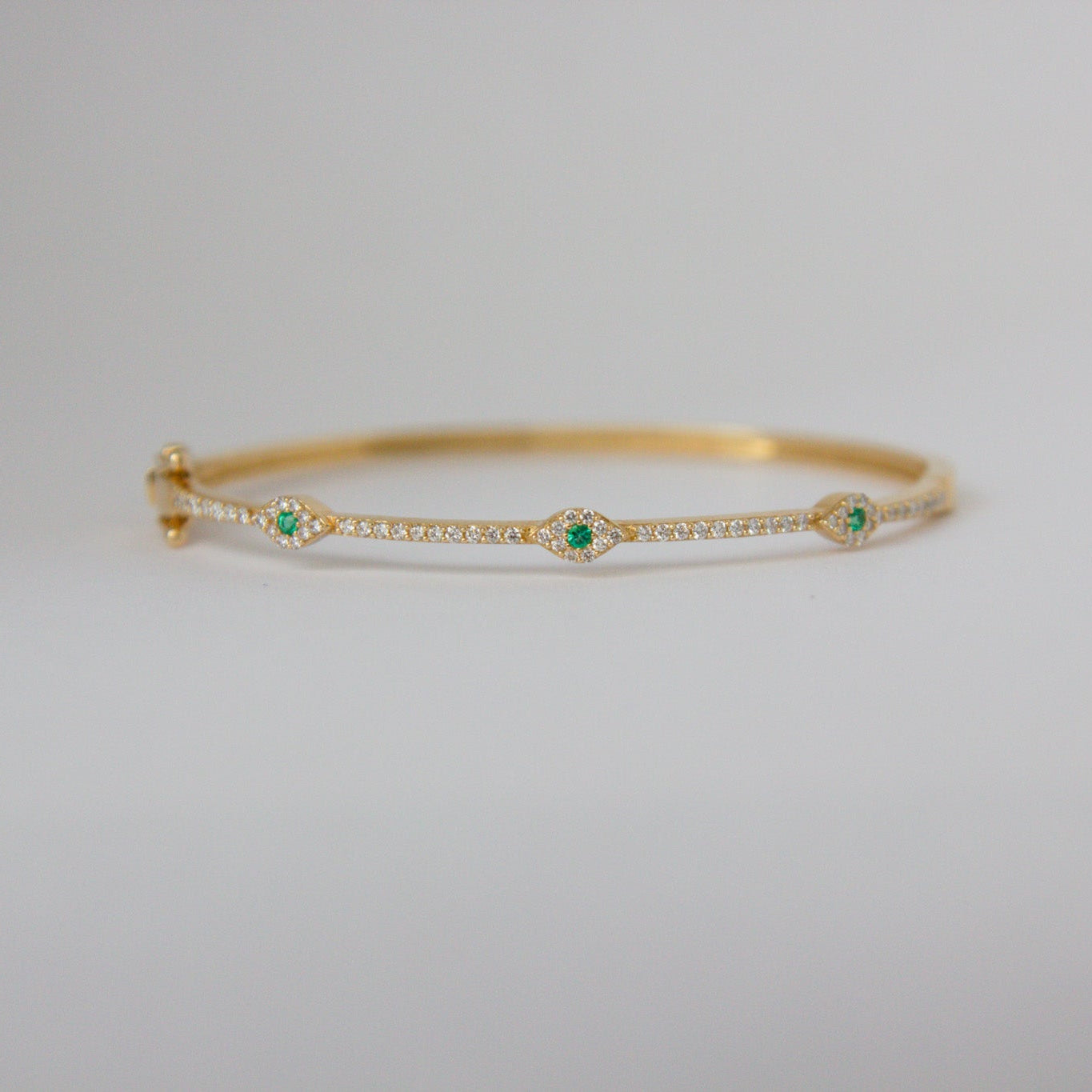 Gold bracelet with green gemstones on a light gray background
