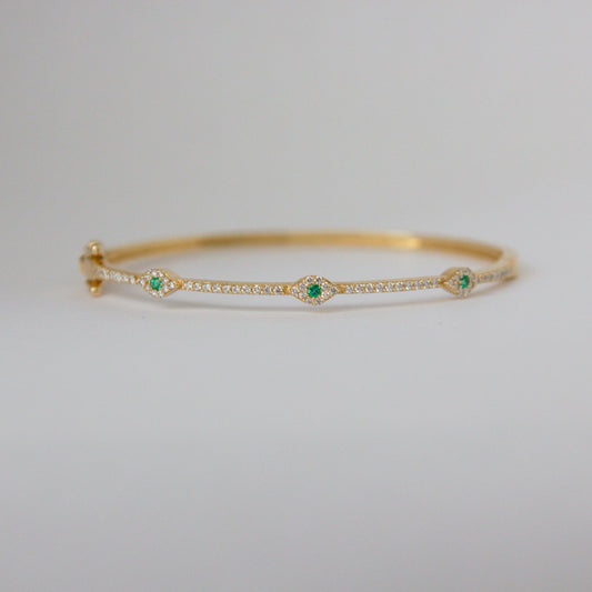 Gold bracelet with green gemstones on a light gray background