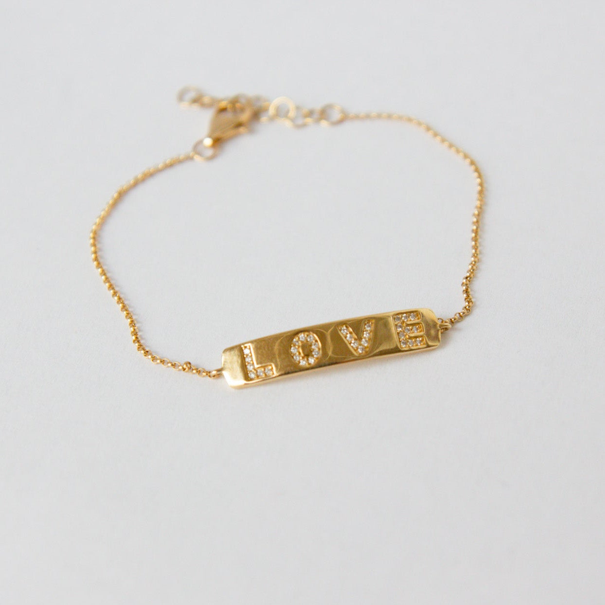 Gold bracelet with 'LOVE' engraving on a light gray background
