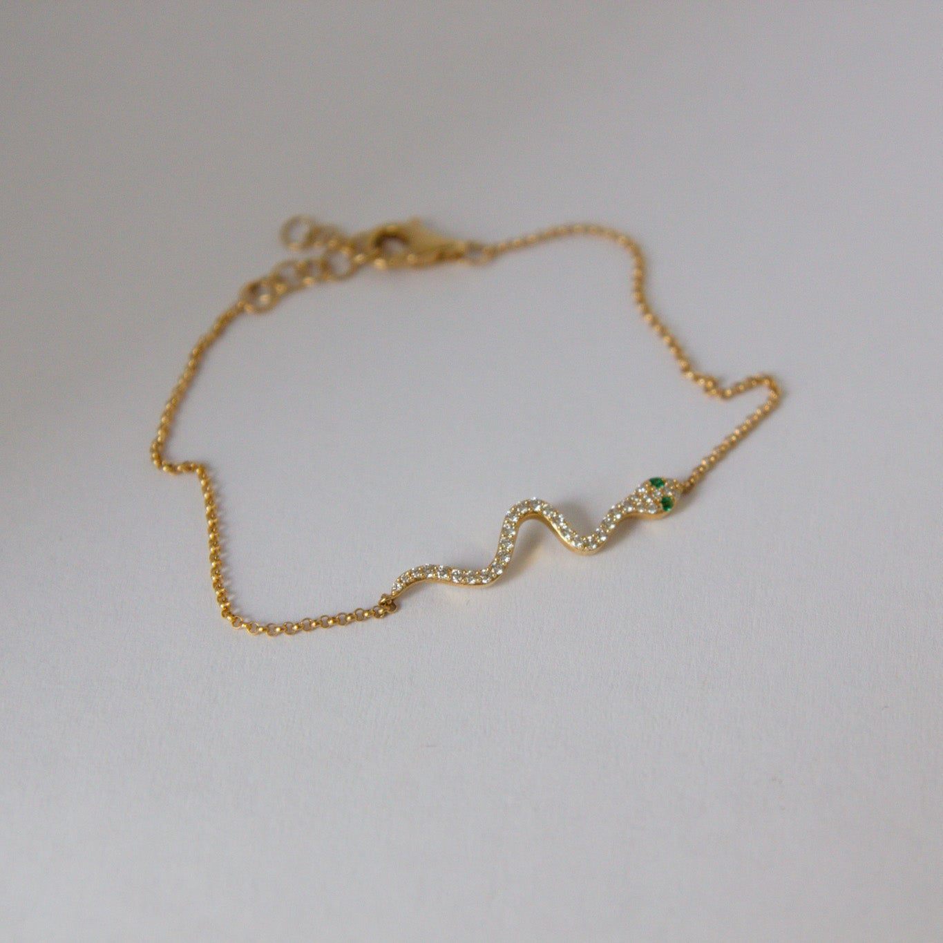 Gold bracelet with a green gemstone on a light gray background