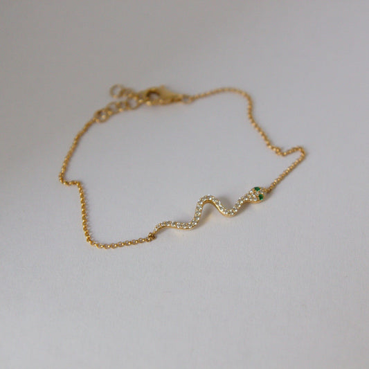 Gold bracelet with a green gemstone on a light gray background