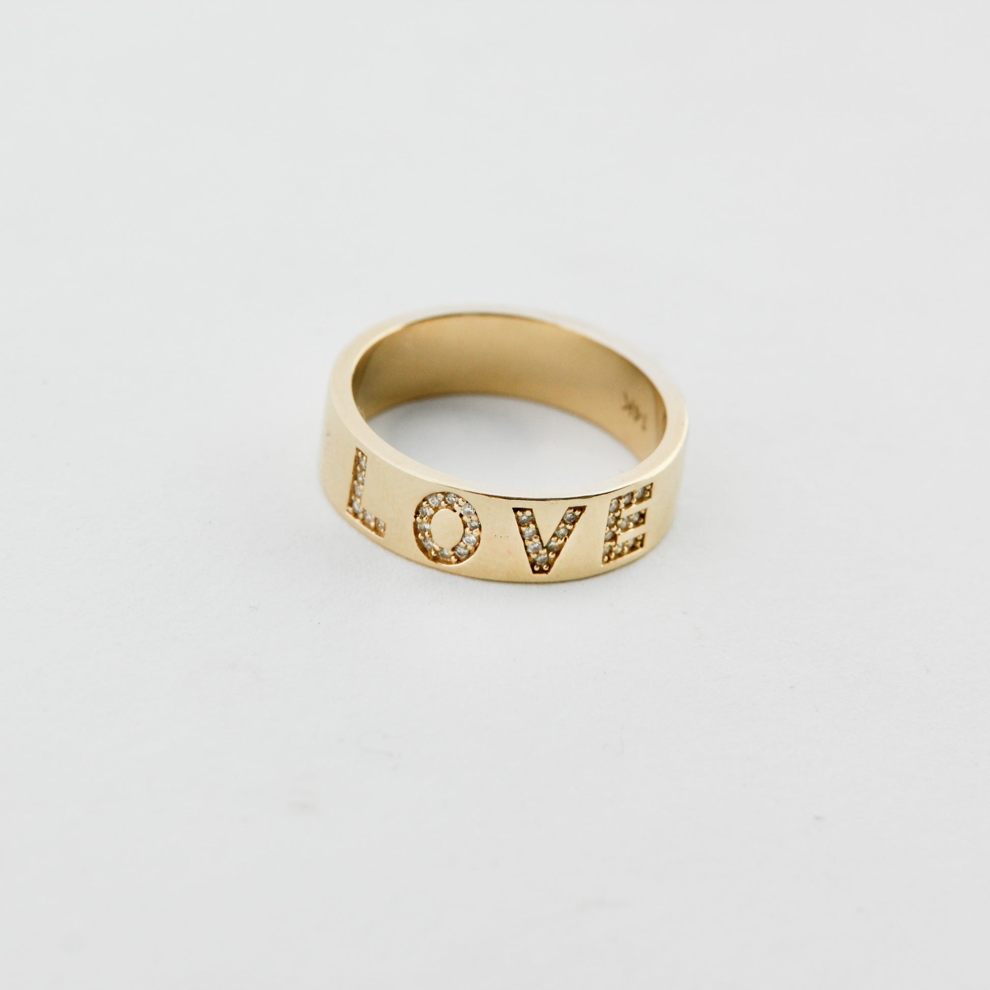 Gold ring with 'LOVE' engraving on a light gray background