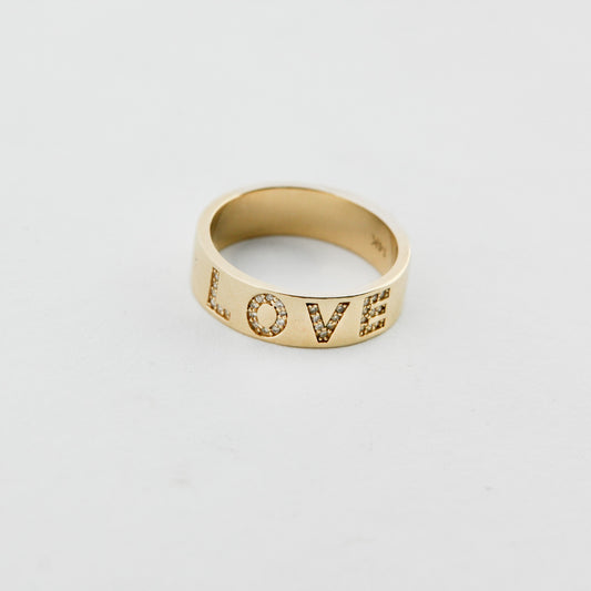 Gold ring with 'LOVE' engraving on a light gray background