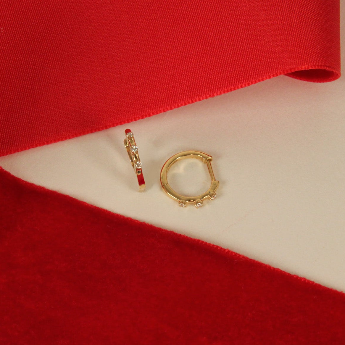 Two gold earrings with three diamonds on a red and white fabric background