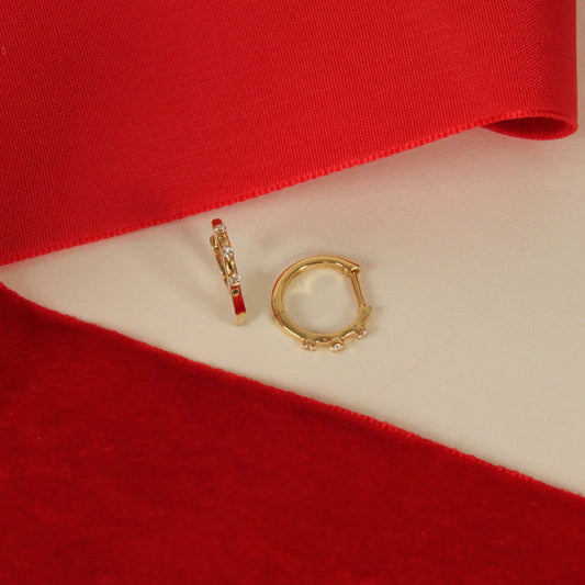 Two gold earrings with three diamonds on a red and white fabric background