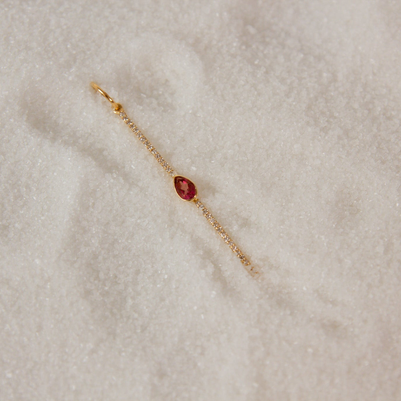 Gold charm with a pink sapphire  teardrop gemstone on snow