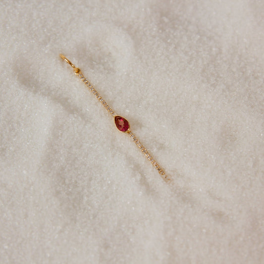 Gold charm with a pink sapphire  teardrop gemstone on snow