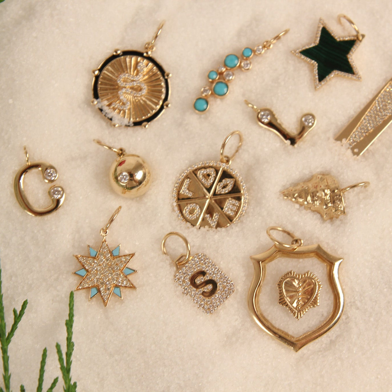 Collection of gold and silver jewelry pendants on a textured beige surface with greenery.